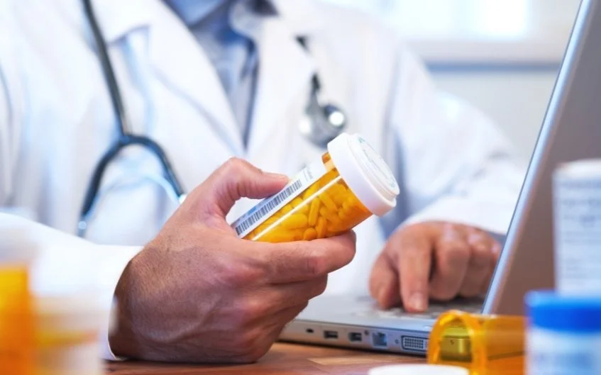 A doctor hold some pills in his hands and using laptop
