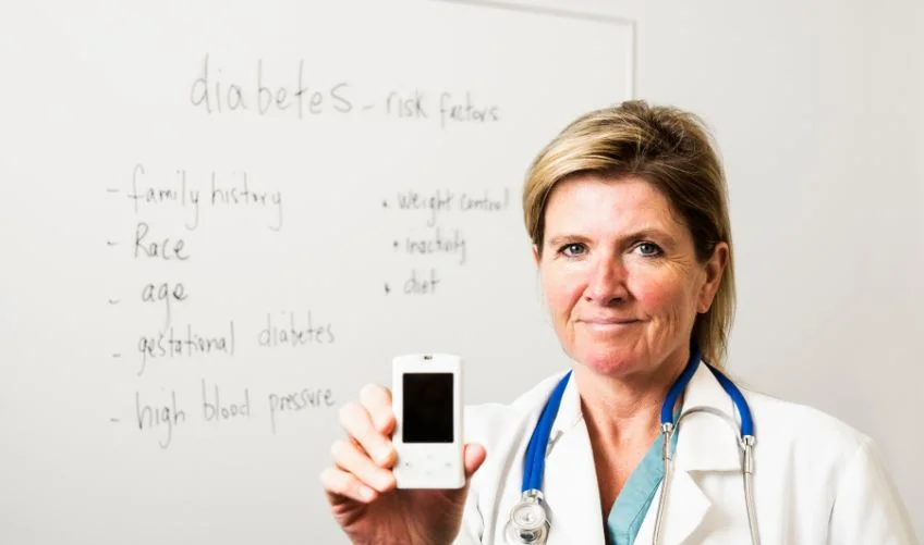 A female endocrinologist or doctor with diabetes risk factors written on the whiteboard behind her.
