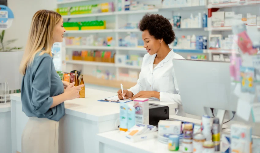 The female cashier in a white coat serves the customer.